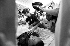 28日，兇手門多薩身著警服躺在棺木里。