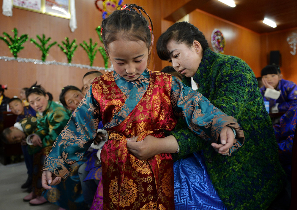 2月27日，在西藏自治區(qū)兒童福利院，來(lái)自拉薩市尼木縣的“愛(ài)心媽媽”德慶旺姆（右）在為來(lái)自那曲地區(qū)的嘎瑪曲宗換上節(jié)日盛裝。